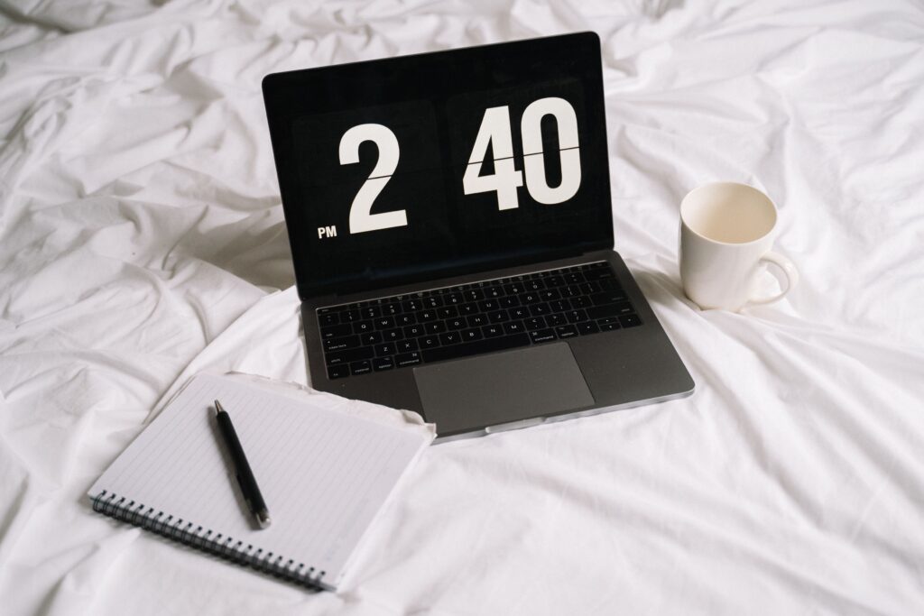 Laptop displaying a time, specifically 2:40 p.m. beside with notebook, pen and coffee mug.